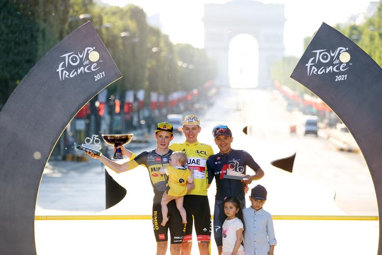Jonas Vingegaard (t.v.) med datteren Frida på armen nyder karrierens største øjeblik på Champs-Élysées. sammen med konkurrenterne Tadej Pogacar og Richard Carapaz.
 Foto: Garnier Etienne/Ritzau Scanpix