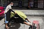 Denne mand faldt torsdag om på en gade midt i Bangkok. Det er uvist, om årsagen var coronarelateret. I flere timer prøvede forbipasserende at tilkalde en ambulance, men kunne ikke komme igennem til alarmcentralerne, der med flere tusinde coronaopkald om dagen er lagt ned. I stedet forsøgte beboere i gaden at mindske mandens lidelser en smule ved at skærme ham for den skarpe sol. Foto: Claus Blok Thomsen