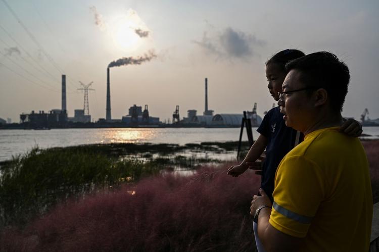 En far og hans datter ved bredden af Huangpu-floden i Shanghaii, hvor de ser over på et kraftværk. Stigende kulpriser har ført til, at mange kraftværker har skåret ned på deres produktion af elektricitet.    Foto: Hector Retamal/Ritzau Scanpix