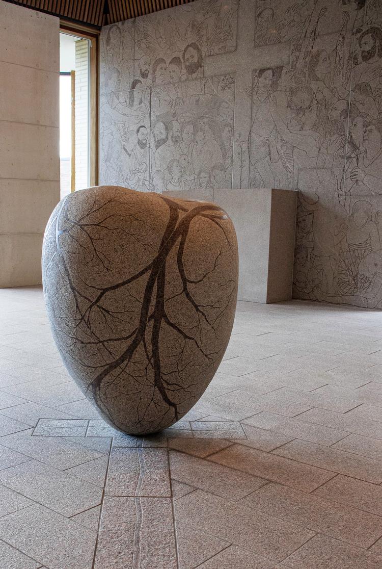 Fra Gødstrup Hospitalskirke. I forgrunden den hjerteformede døbefont, med blodkar, i baggrunden kirkens altertavle. Foto: Laila Westergaard