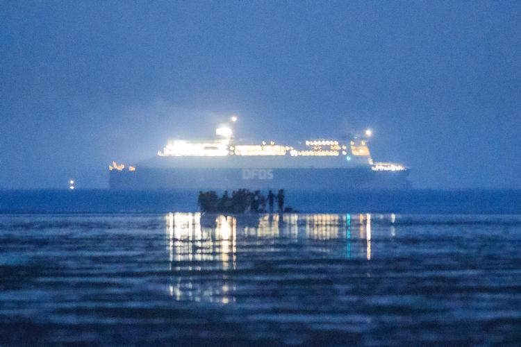 På dette foto fra 22. september sidste år ses en gruppe migranter på stranden ved Gravelines i det nordlige Frankrig, mens en dansk DFDS-færge sejler i Den Engelske Kanal i baggrunden.  Foto: Sameer Al-doumy/Ritzau Scanpix