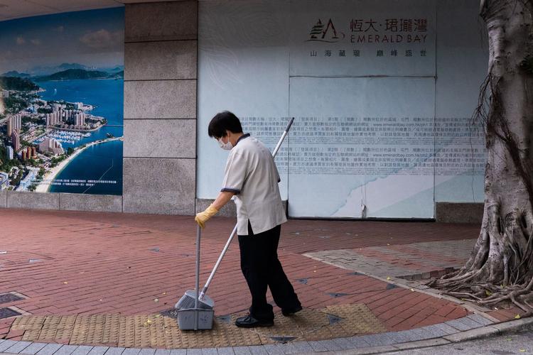 En kvinde gør rent foran en lejlighedskompleks i Emerald Bay, Hongkong. Bygningen er et af ejendomsgigantens Evergrandes mange projekter.  Foto: Bertha Wang/Ritzau Scanpix