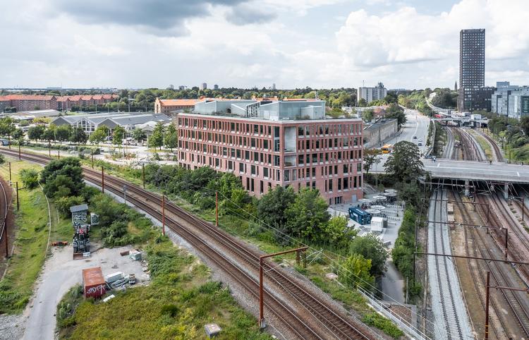 Det bliver ikke meget mere urbant med bil- og tog-trafik til alle sider. Atriet er smukt og varmt beklædt med stave og plader af fyrretræ. Store træer i potter og danske møbelklassikere er med til at sikre en hjemlig stemning. Foto: Poul Christensen