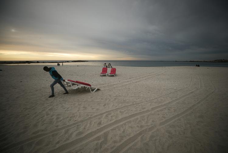 En mand pakker solstole sammen ved Camps Bay Beach i Sydafrika. Netop de afrikanske landes befolkninger har fået markant færre vaccinationer mod coronavirus. Det står i skærende kontrast til mange vestlige lande, hvor vaccinetilslutningen er oppe på 80-90 procent. »En skandale«, kalder WHO’s generaldirektør, Tedros Adhanom Ghebreyesus den skæve fordeling. Foto: Mike Hutchings/Ritzau Scanpix
