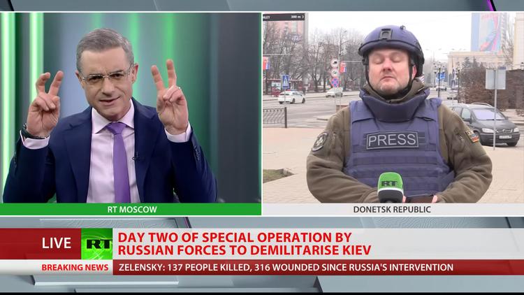 På mange måder minder RT UK om tilsvarende nyhedskanaler som TV 2 News. Det er værtsbåret tv, hvor der stilles om til såvel eksperter  som journalister i marken. Her er det fredag middag dansk tid og en journalist er igennem fra Donetsk.  Bemærk at  kanalen ikke kalder det en krig, men bruger ordene ’Specialoperationen til at demilitarisere Kiev’.    Foto: Screendump fra RT UK