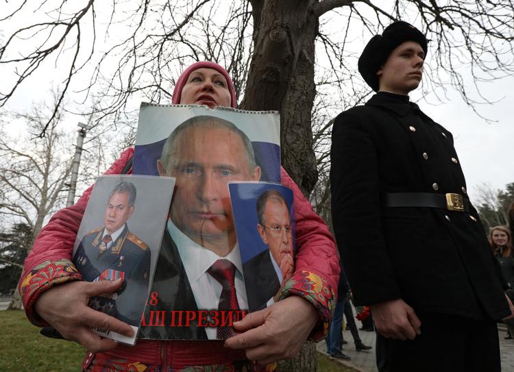 En kvinde omfavner skilte med præsident Vladimir Putin, forsvarsminister Sergei Shoigu og udenrigsminister Sergei Lavrov i byen Sevastopol i den russiskannekterede halvø Krim. Anledningen er festdagen for forsvar af fædrelandet den 23. februar. Både Putin og Lavrov kan være omfattet af immunitet i Den Internationale Straffedomstol ICC, mener en ekspert. Foto: Alexey Pavlishak/Ritzau Scanpix