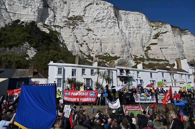 People hold banners and placards during a demonstration against the sacking of 800 P&amp;O workers near the Port of Dover on the southeast coast of England on March 18, 2022. - P&amp;O Ferries, which sails daily between Britain and France, axed 800 UK crew with immediate effect and suspended services in a bid to stay afloat, sparking protests from angry staff and trade union fury. The Dubai-owned group announced it has shed more than one quarter of its staff in a drastic restructuring to save cash, and halted services for the next few days. (Photo by Glyn KIRK / AFP) Foto Glyn Kirk