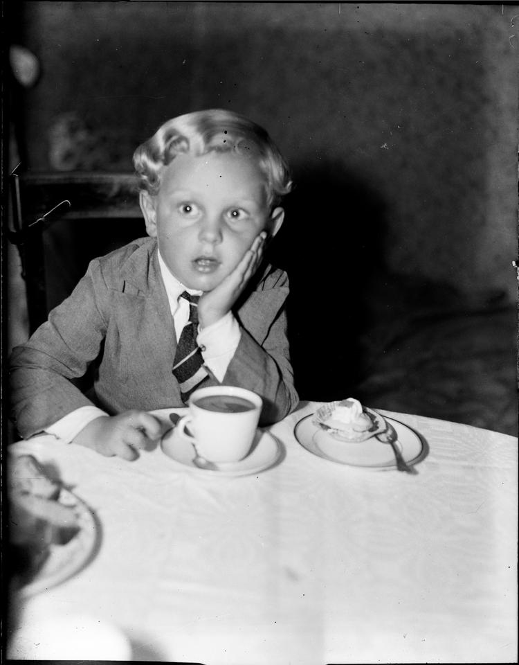 En lille dreng i sit stiveste puds får sig en kage og lidt kaffe omkring år 1930. Den var dog ikke gået, hvis det stod til John Locke. 1600-tals-filosoffen frarådede på det kraftigste alle former for »sukkerstads«, i særdeleshed til børn, men sådan set også til voksne. Han var også imod meloner, blommer, druer og ferskener, for de havde en »tillokkende smag i en meget usund saft«. Pærer, bær og især æbler derimod tager ingen skade af, skriver han i 'Tanker om opdragelsen' fra 1693. Foto: Tage Christensen