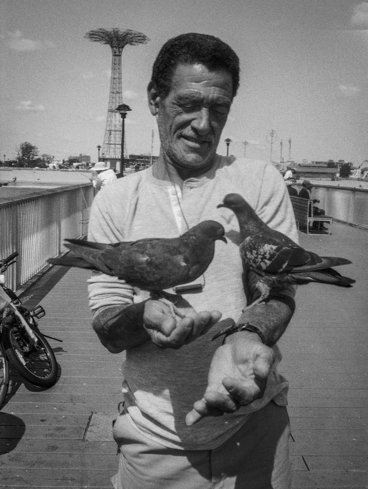 Man on Pier with Two PigeonsMandatory credit: Coney Island People 50 Years, 1970-2020 by Harvey Stein is published by Schiffer. The photographs are copyright Harvey Stein.Please include the following links:https://www.harveysteinphoto.com/coney-island-people-50-years-bookhttps://schifferbooks.com/collections/schiffer/products/coney-island-people?_pos=1&amp;_sid=fa06a2f4d&amp;_ss=r Foto: Coney Island People 50 Years, 1970-2020 by Harvey Stein is published by Schiffer. The photographs are copyright Harvey Stein.