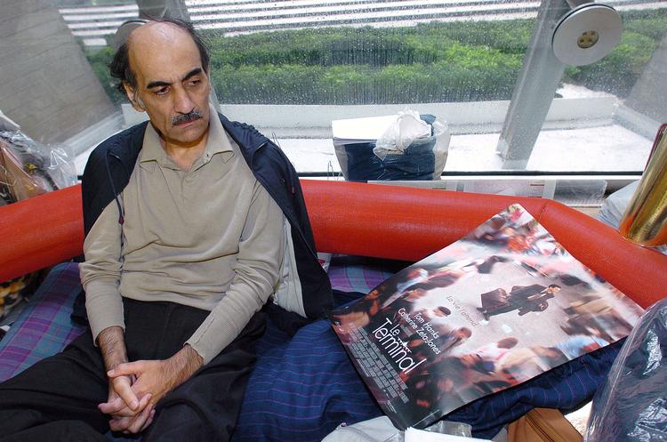 Mehran Karimi Nasseri fotograferet i 2004 i Charles de Gaulle-lufthavnen i Paris, mens han kigger på en plakat med den film, hans liv dannede grundlaget for.  Foto: Stephane De Sakutin/Ritzau Scanpix