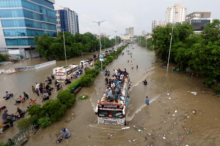 Mennesker sidder på taget af en bus, mens andre vader igennem vandmasserne efter store oversvømmelser i Pakistan dette efterår. Foto: Akhtar Soomro/Ritzau Scanpix