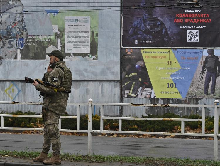 En ukrainsk politibetjent taler i telefon ved siden af en plakat, der opfordrer alle i Kherson til at fordømme personer, som kollaborerede med russerne. Foto: Genya Savilov/Ritzau Scanpix