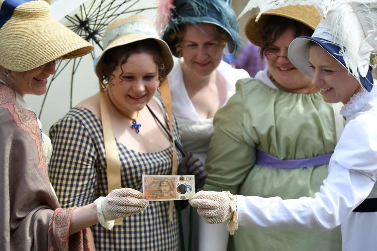 Jane Austen-fans samles i selskaber verden over for at dyrke hendes arv. Her ses folk i kostume beundre en pundseddel med Jane Austens billede. Foto: Pool/Ritzau Scanpix