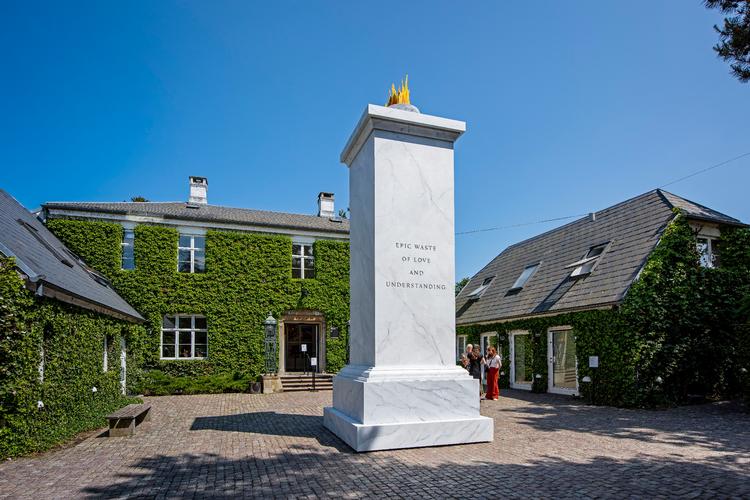 Som en stor, firkantet fallos troner træsøjlen op foran Louisianas hovedindgang - med en lille gylden flamme som kronen på værket, der hedder 'EPIC WASTE'. Foto: Louisiana - Poul Buchard / Brøndum & Co