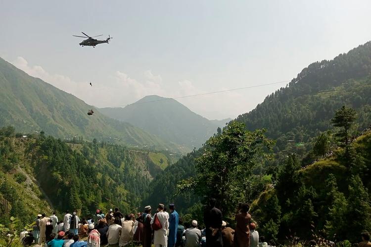 Lokale kigger på, mens en soldat hængende fra en militærhelikopter forsøger at nå ned til de otte personer, der sidder fast i en lift i landsbyen Pashto i det nordlige Pakistan. Foto: Prateek Kumar/Ritzau Scanpix