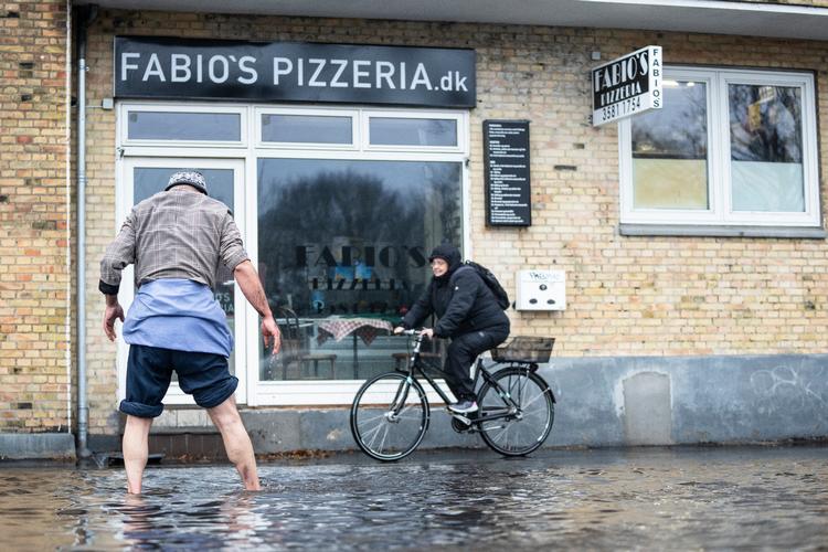Aboud Al-Hilw forsøger at rense afløbet, som på grund af den megen regn er godt stoppet til på Tagensvej i København torsdag. Aboud var på vej fra Østerbro mod Nordvest for at hente sin søn fra skole, men da han kommer forbi massive vandmængder på Tagensvej, beslutter han sig for at smøge bukserne op og tage initiativ. Foto: Thomas Traasdahl/Ritzau Scanpix