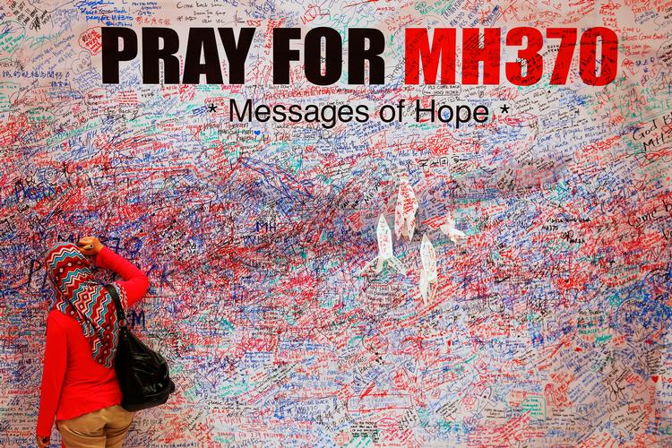 En kvinde skriver en besked på en plakat i det centrale Kuala Lumpur til støtte for passagerene på det forsvundne fly MH370 samt deres efterladte. Foto: Damir Sagolj/Ritzau Scanpix