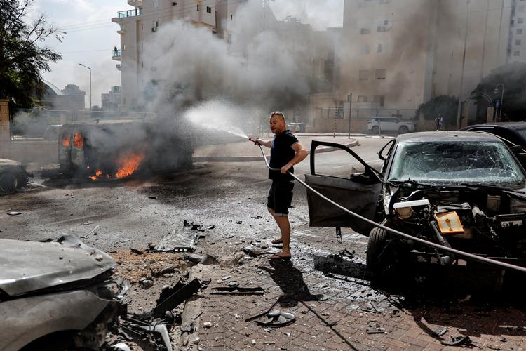 En mand i den israelske by Ashkelon forsøger at slukke branden i en bil, efter at den er blevet ramt af raketter affyret fra Gaza under Hamas' store angerb 7. oktober.  Foto: Ammar Awad/Ritzau Scanpix