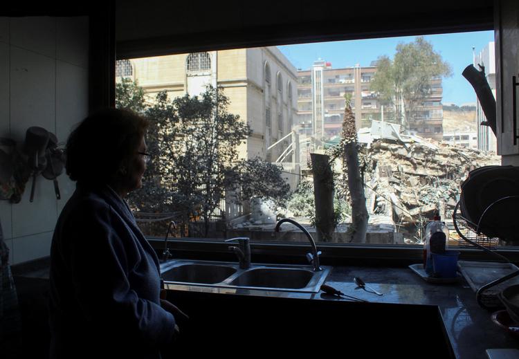 Wafaa Badawi, universitetsprofessor, kigger ud af sit køkkenvindue i Syriens hovedstad, Damaskus, mod Irans konsulat, der mandag blev ramt af et israelsk missil og lagt i ruiner. Den iranske ambasssade ved siden af står uskadt. Foto: Firas Makdesi/Ritzau Scanpix