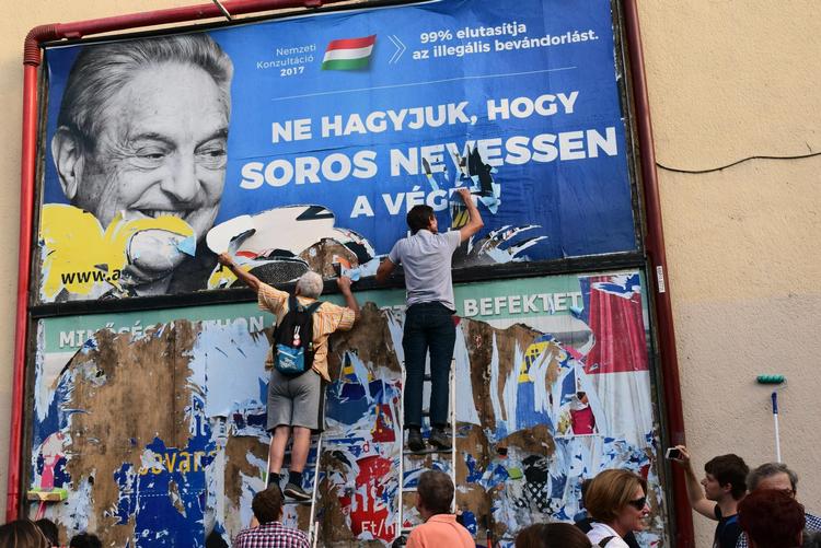 Ungarns regering har iværksat en kampagne mod finans-manden George Soros, som i deres optik har for stor indflydelse. På billedet ses Soros-støtter fjerne en af kampagnens plakater. 