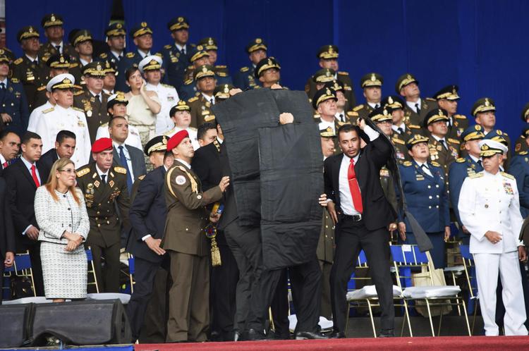Her har attentatet lige fundet sted. Præsident Nicolas Maduro er dækket af sikkerhedsfolkenes skjolde. Mange kigger nervøst op i luftten.  Xinhua/AP