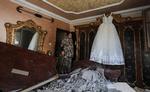 En palæstinensisk kvinde vender hjem til sin bolig, hvor der ligger en bunke murbrokker på gulvet efter et israelsk luftangreb. Men kjolen klarede skærene.   Mahmud Hams/AFP/Ritzau Scanpix