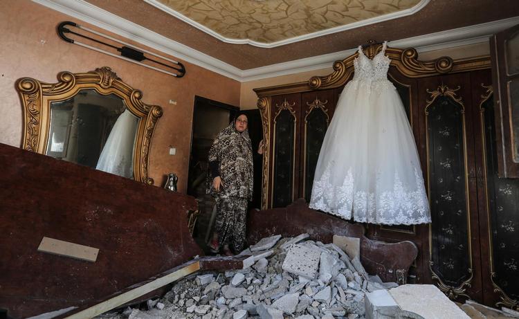 En palæstinensisk kvinde vender hjem til sin bolig, hvor der ligger en bunke murbrokker på gulvet efter et israelsk luftangreb. Men kjolen klarede skærene.   Mahmud Hams/AFP/Ritzau Scanpix
