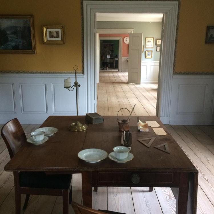 Man skulle næsten tro, at Kamma Rahbek netop havde forladt stuerne for at hente teen. Ud over te og måltider, var det firkantede bord stedet, hvor tidens store forfattere og debattører mødtes for at diskutere litterære og politiske spørgsmål. 