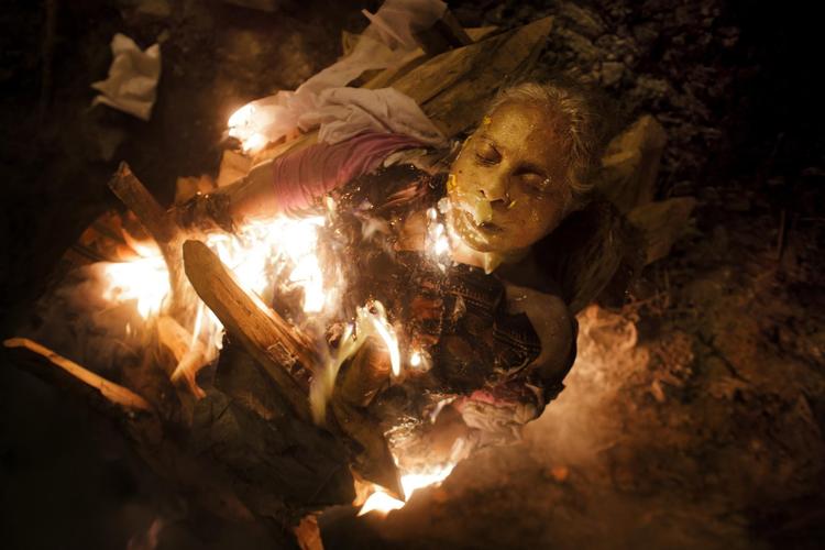 Indien. En brahminsk kvinde brændes på Manikarnika Ghat i Varanasi i Indien. I hinduismen er døden en overgang fra ét liv til det næste. Vi fødes på ny igen og igen i det store hjul, samsara. Målet er er den evige moksha - altså udfrielsen fra samsara. Dør man, og bliver man brændt i den nordindiske by Varanasi, kan man opnå moksha med det samme. I hinduismen brændes kroppen, fordi ild renser, og der må ikke være jordiske rester, som kan tynge sjælen og holde den tilbage fra rejsen videre. Manikarnika Ghat i Varanasi er en af de ældste og helligste ghats i Indien. Røgen hænger tykt over den offentligt tilgængelige plads, mens ligbålene brænder.  