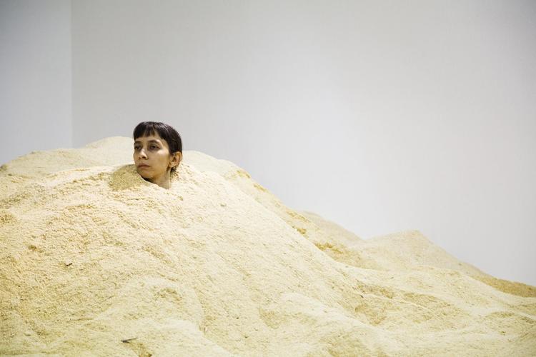 Den chilenske kunstner Regina José Galindo sidder midt i en selvskabt ørken af savsmuld. 