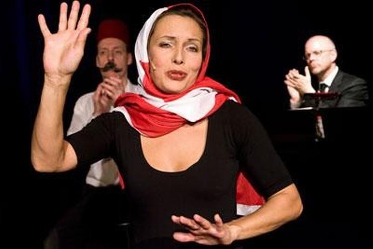 I en mellemøstlig udgave af Sebastians gamle sang om den stiltiende malkeko bruger Mette Marckmann Dannebrog som muslimsk hijab. 