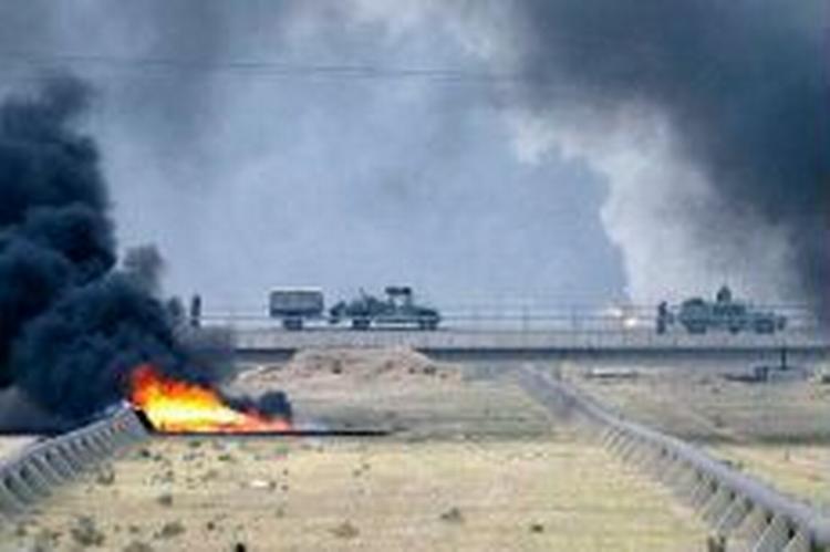 En amerikansk militærkonvoj passerer en brændende olierørledning nær Iraks næststørste by, Basra. - Foto: AP 