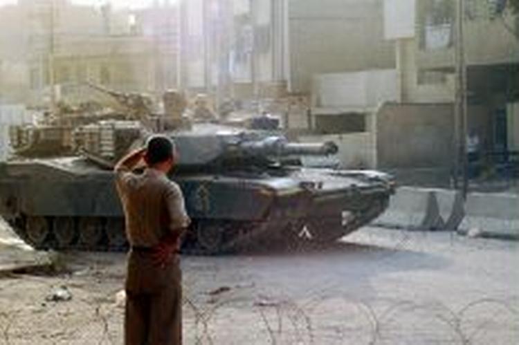 En irakisk dreng ser en amerikansk tank køre forbi en vejspærring i Bagdad. - Foto: AP 