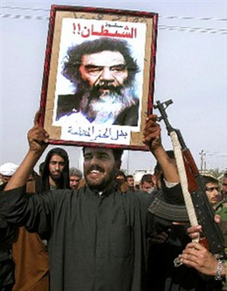Medlemmer af den proiranske al-Da wa parti fejrer Saddam Husseins tilfangetagelse. Over billedet står  Djævlens fald . Nedenunder  De sorte hullers helt .   Foto: Nabil Aljurani/AP 