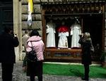 Forbipasserende ser på vinduet i Gammarellis skrædderforretning i Rom, hvor tre størrelser af pavedragten er udstillet.   Foto: Peter Dejong/AP 