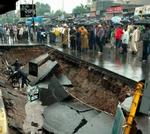 Indbyggere samles om et gigantisk hul i vejen i byen Ahmadabad, der er blevet hærget af vandmasserne. - Foto: AP 
