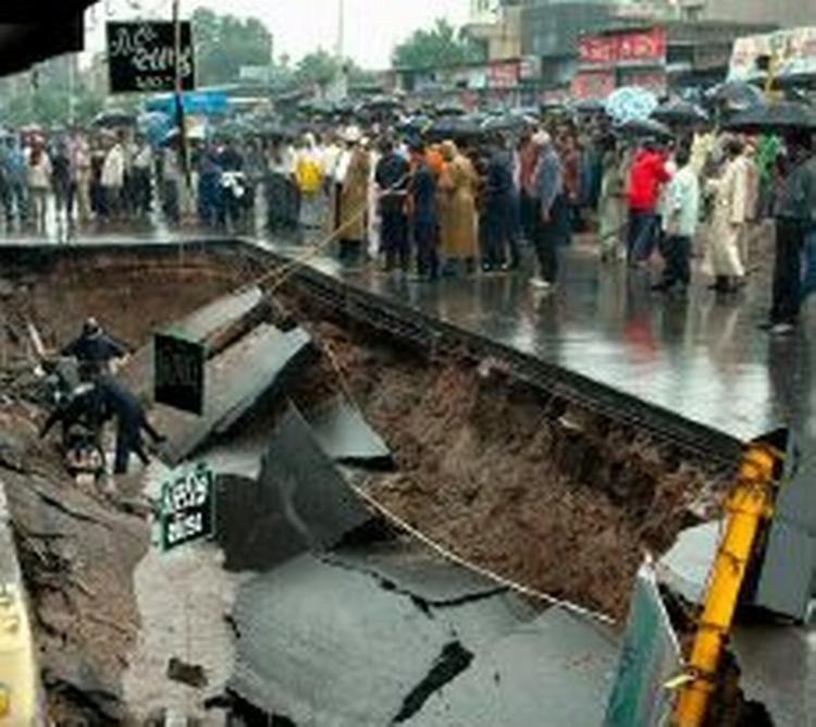 Indbyggere samles om et gigantisk hul i vejen i byen Ahmadabad, der er blevet hærget af vandmasserne. - Foto: AP 