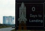 'O dage til landing', står der fortsat på skiltet uden for Kennedy Rumcentret i Cape Canaveral. Skyet vejr i området forhindrede i går landing. - Foto: AP 