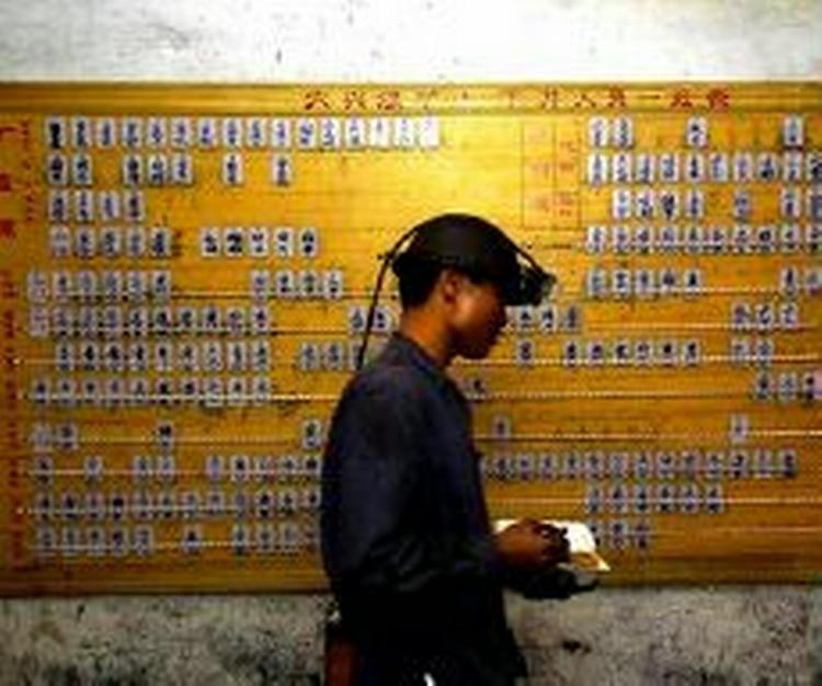 En redningsmedarbejder passerer forbi listen over de minearbejdere fra Daxing-minen i Guangdongprovinsen i Kina. 123 af dem er stadig savnet og formodes druknet.   Foto: Liu Dawei/AP 
