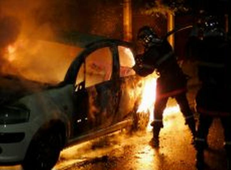 En brandmand forsøger at slukke en brændende bil under optøjerne i nat. - Foto: AP 