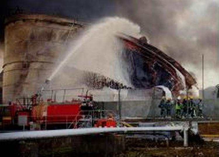 Brandfolk forsøger at nedkøle en af de brændende olietanke med skum. - Foto: AP 