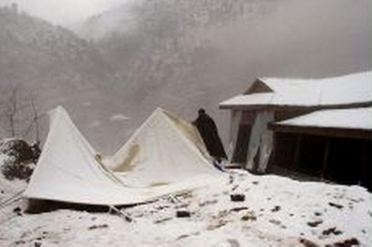 En mand forsøger at rejse familiens telt op i Awan Patti i Jhelum dalen i Kashmir. Jordskælvsområdet oplevede i dag de heftigste regn- og snefald hidtil i denne pakistanske vinter. - Foto: AP 