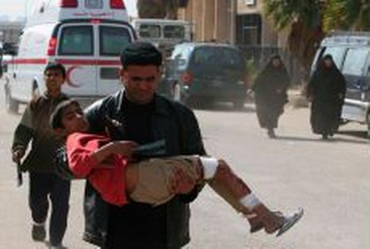En irakisk mand bærer en såret dreng væk efter en af de eksplosioner, der i dag ramte Bagdad. - Foto: AP 