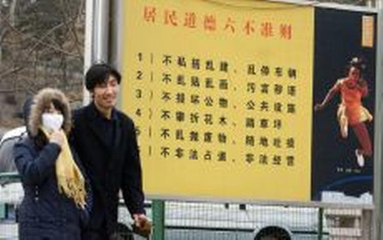 Et kinesisk par går forbi en liste over 'gadeadfærd', der ikke længere tillades i Beijing. Spytteriet er det første, der bliver gjort op med. - Foto: AP 