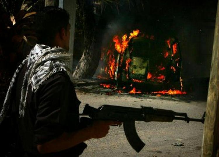 En palæstinsisk politmand går fordi en brændende bil i Gaza i dag, hvor politiet var i kamp mod Hamas-folk. - Foto: AP 