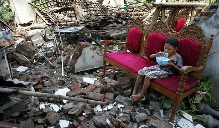 En lille dreng får en skål ris i ruinerne i en landsby i Bantul-distriktet. - Foto: AP 