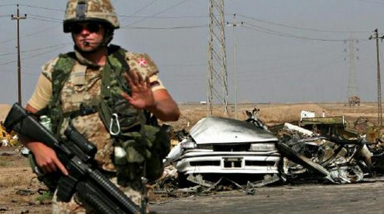En dansk soldat bevogter vejen, hvor en bil er blevet sprængt i stykker i Basra 20. april. De danske tropper får en central placering i koalitionen i Irak, mens andre lande reducerer styrkerne. - Arkivfoto: AP 