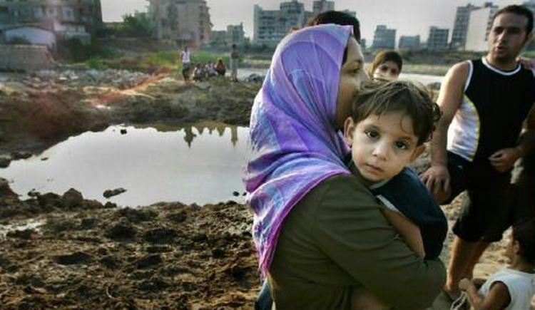En kvinde med et barn ved et af de bombekratere, som israelske granater har efterladt i byen Tyre i det sydlige Libanon. - Foto: AP 