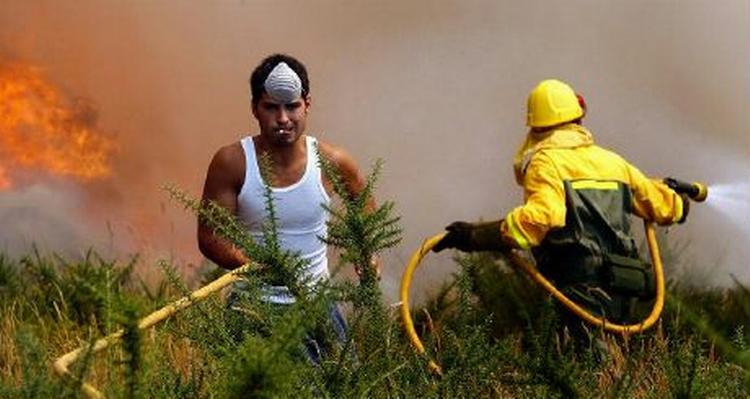 En indbygger med en smøg i munden hjælper en af redningsarbejderne med at slukke branden i det nordvestlige Spanien. - Foto: AP 