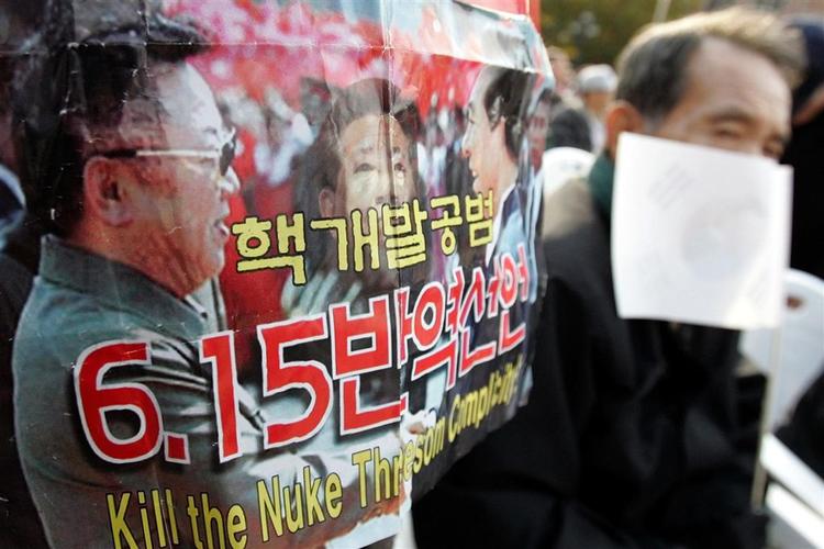 A Korean War veteran sits next to a poster featuring North Korean Leader Kim Jong Il, left, South Korean President Roh Moo-hyun, center, and former President Kim Dae-jung during an anti-government rally against North Korea's nuclear program, in Seoul, Friday, Nov. 10, 2006. Chief envoys from South Korea, Japan and the United States will discuss North Korea's nuclear program on the sidelines of an Asia-Pacific Economic Cooperation meeting next week in Vietnam, the Yonhap news agency said Friday. The letters read "Abolition of June 15 inter-Korean Joint Declaration and resignation of President Roh Moo-hyun."  (AP Photo/ Lee Jin-man) 